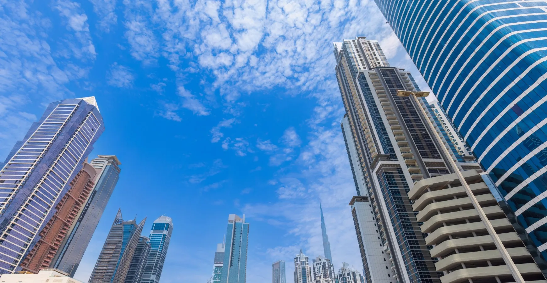 A low-angle panoramic view looking up at modern skyscrapers against a blue sky with light clouds, representing business expansion and corporate Marketing Solutions.
